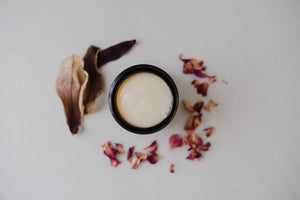Small jar of cream surrounded by dry rose and magnolia petals